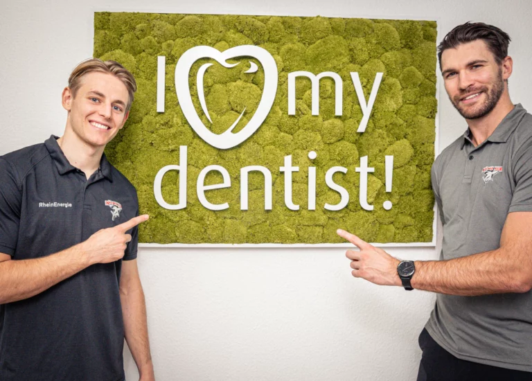 Zwei Spieler der Kölner Haie vor dem I love my dentist-Schild