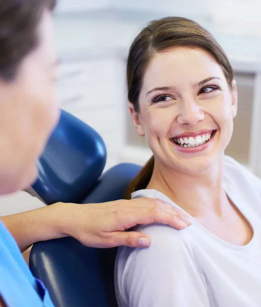 Eine lachende Frau nach einer Wurzelspitzenresektion blickt auf ihre Zahnärztin