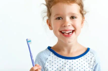 Ein Kind welches in die Kamera lächelt und eine Zahnbürste in der Hand hat
