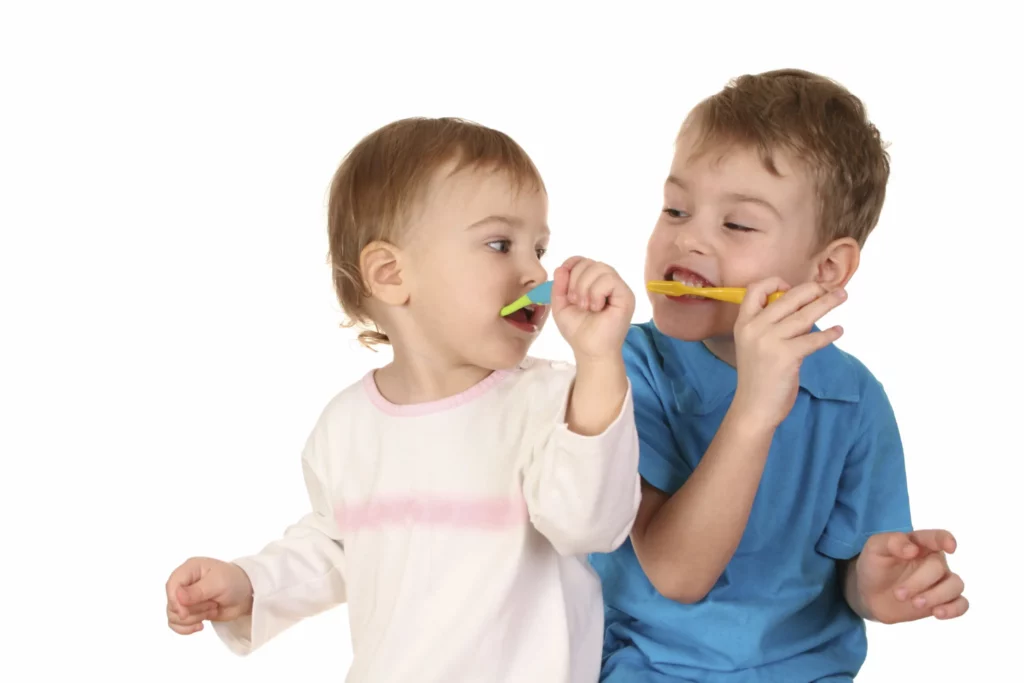 Zwei nebeneinander sitzende Kinde, welche sich die Zähne putzen