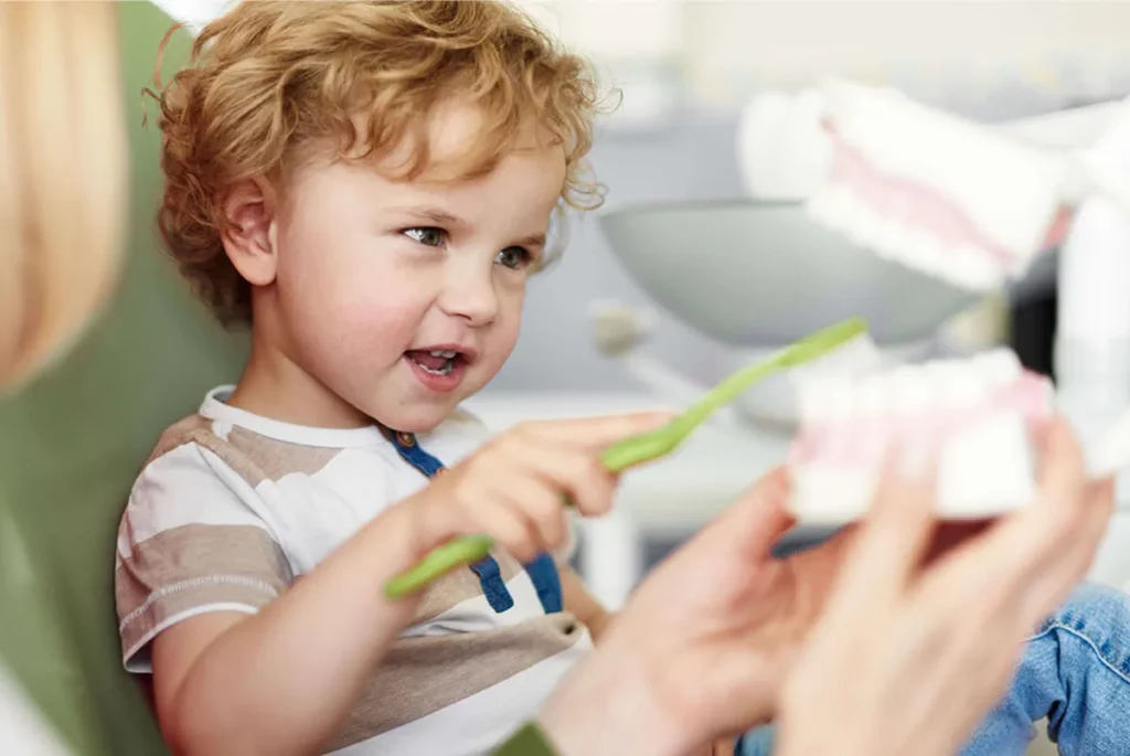 Ein Kind sitzt auf dem Behandlungsstuhl säubert mit einer Zahnbürste ein Gebiss