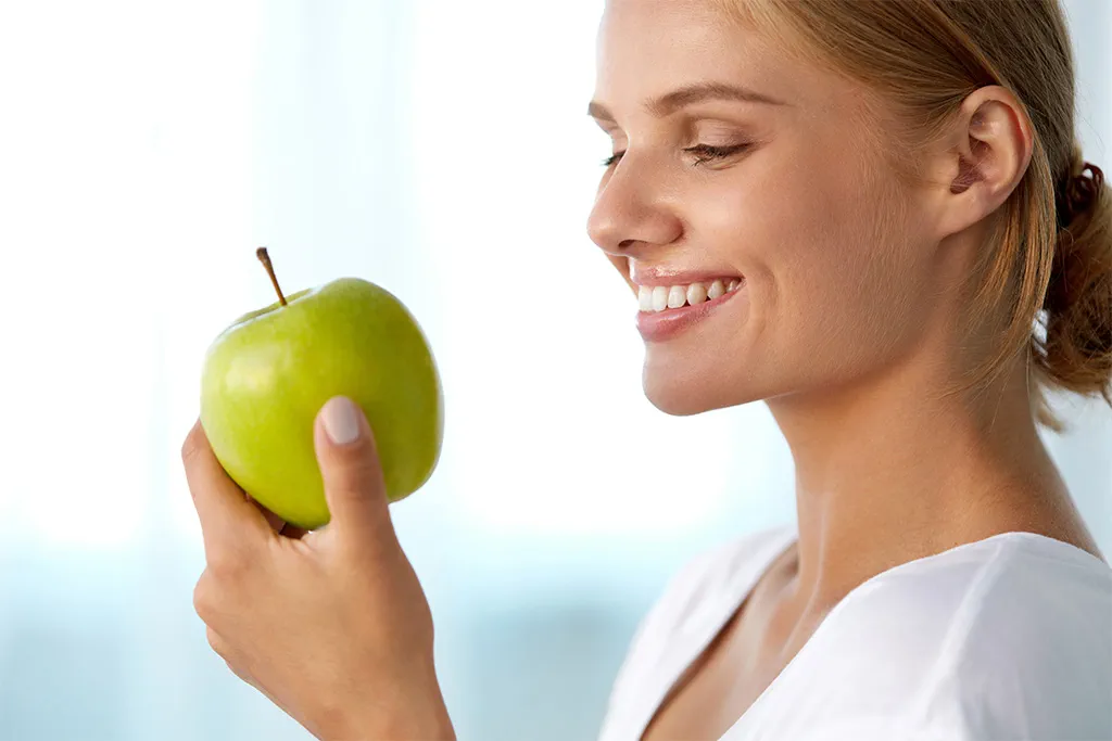 Eine Frau blickt lächelnd auf den grünen Apfel in der Hand