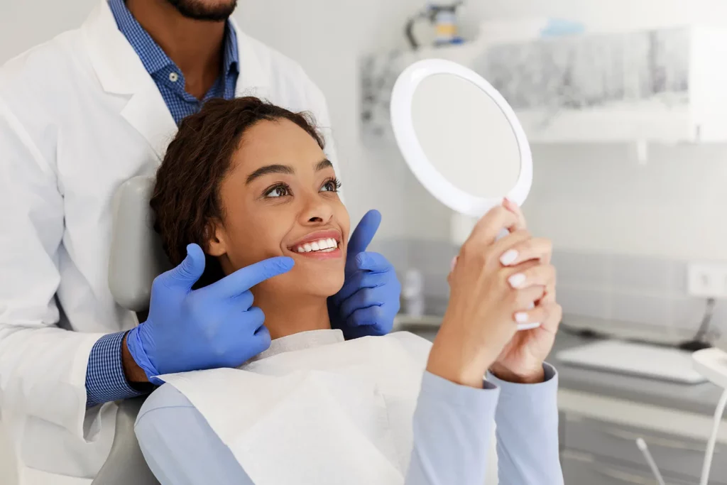 Ein Zahnarzt zeigt seiner Patienten ihre neuen Zähne, welche einen Spiegel in der Hand hält
