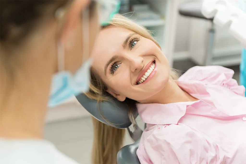 Eine Frau liegt auf dem Zahnarztstuhl und lächelt, davor ist eine Zahnärztin zu erkennen