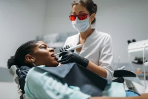 Eine Patientin liegt mit offenem Mund auf dem Zahnarztstuhl, während eine Zahnärztin ihre Zähne versiegelt