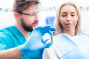 Ein Zahnarzt berät eine Patientin und hält ein Implantat vor ihr.