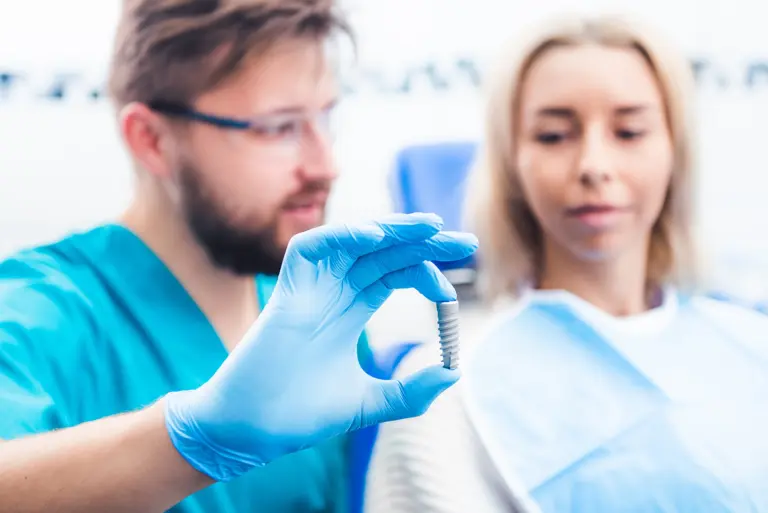 Ein Zahnarzt berät eine Patientin und hält ein Implantat vor ihr.