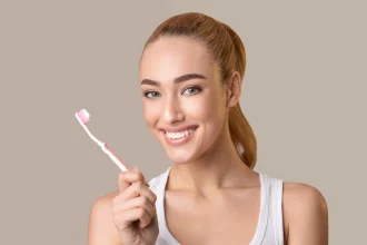Eine lächelnde Frau hat eine Zahnbürste mit Zahnpasta in der Hand